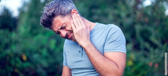 Mann hält sich das Ohr, weil er mit Folgen und Auswirkungen seines Tinnitus zu kämpfen hat.