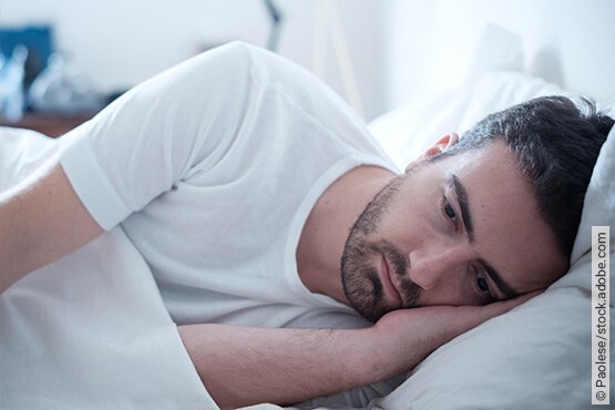 Mann liegt wach im Bett und kann aufgrund der Folgen und Auswirkungen seines Tinnitus nicht mehr schlafen.