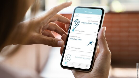 Blick über die Schulter einer Frau auf deren Smartphone mit der aufgerufenen Kalmeda-App.