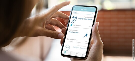 Frau mit Handy in der Hand klickt sich durch die Kalmeda Tinnitus-App.