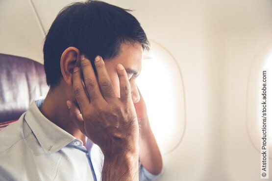 Mann im Flugzeug greift sich an seine Ohren, da veränderte Druckverhältnisse eine Art des Tinnitus auslösen können.