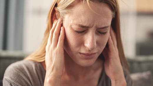 Frau hält sich die Ohren zu, weil sie an chronischem Tinnitus leidet.