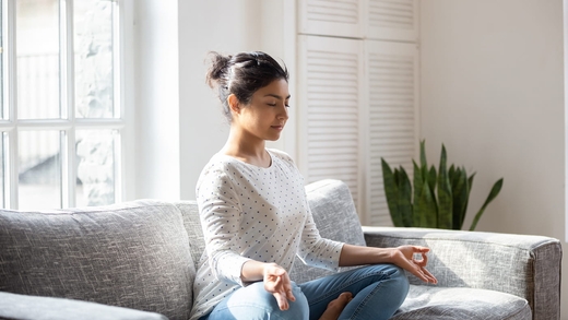 Junge Frau meditiert auf dem Sofa, um die Technik zur Selbsthilfe bei Tinnitus einzusetzen.