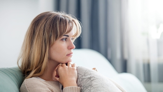 Nachdenkliche Frau sitzt im Wohnzimmer und blickt zur Seite, Symbolbild für Behinderung und die Belastung durch Tinnitus.