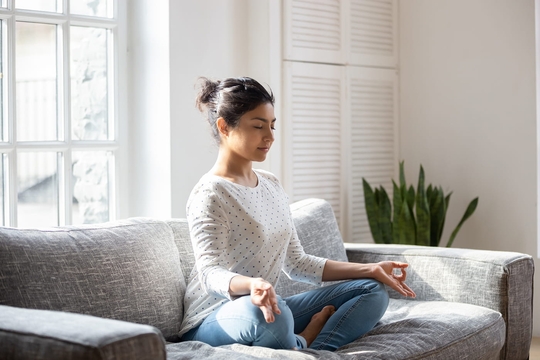 Junge Frau meditiert auf dem Sofa, um die Technik zur Selbsthilfe bei Tinnitus einzusetzen.