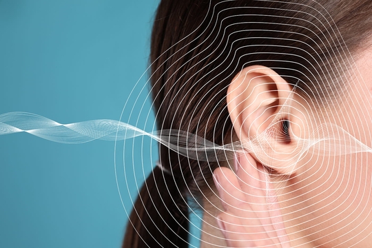 Frau mit Hand am Ohr: Pulsierende Wellen symbolisieren Durchblutungsstörungen als Tinnitus-Ursache.